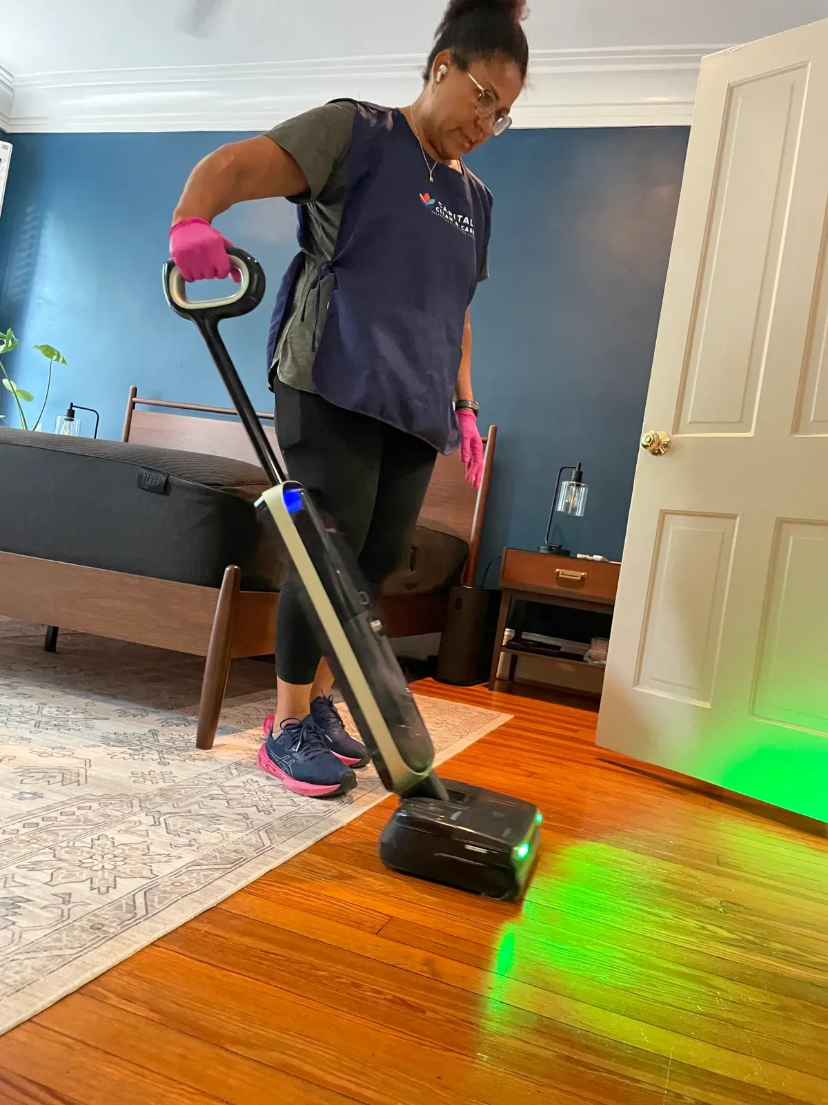 Capital Clean Care crew member running a vacuum with a green floor light across a hardwood floor, the light showing the dust that remains