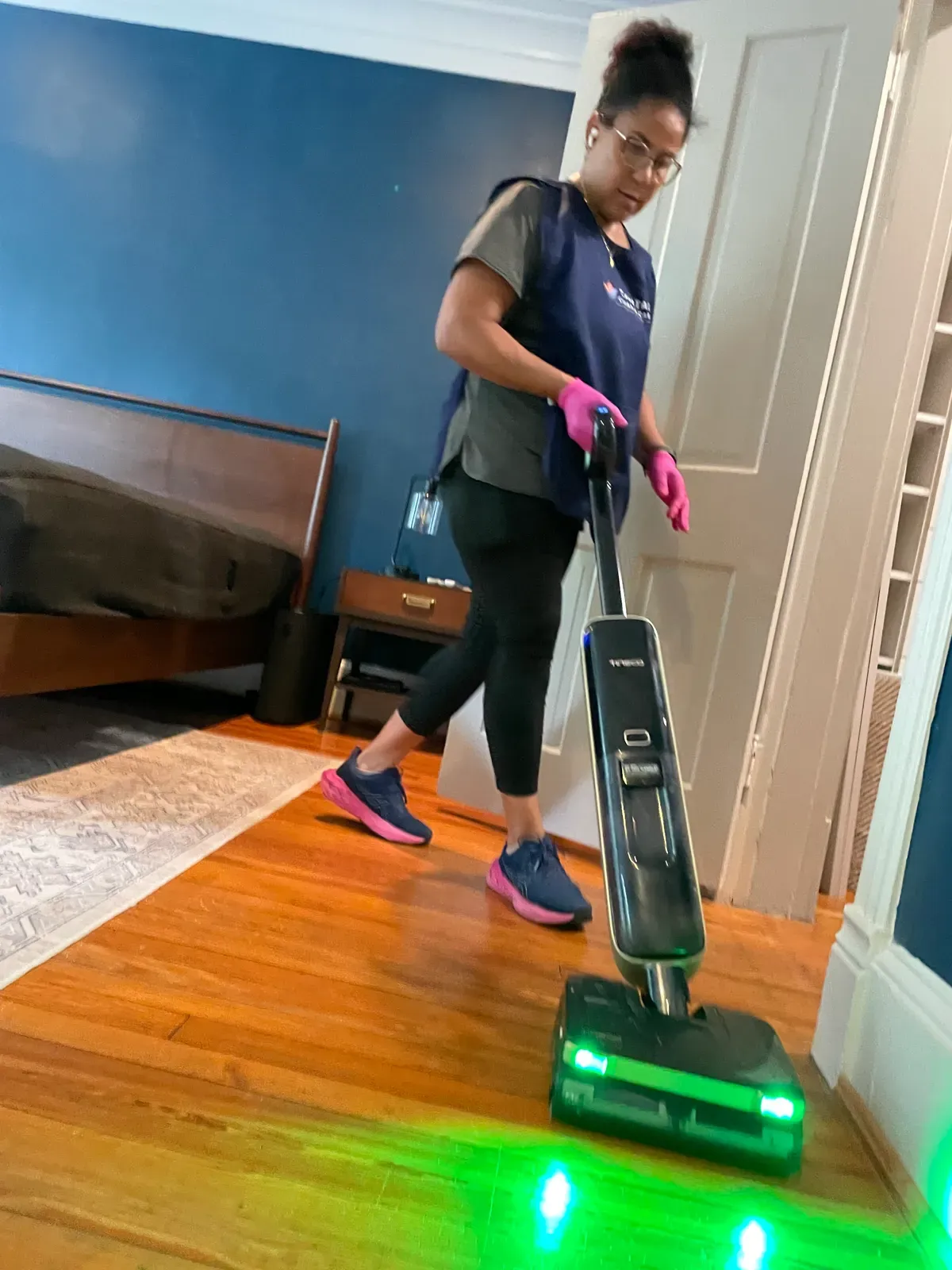 Capital Clean Care crew member vacuuming a hardwood bedroom floor with a headlight vacuum during a cleaning job