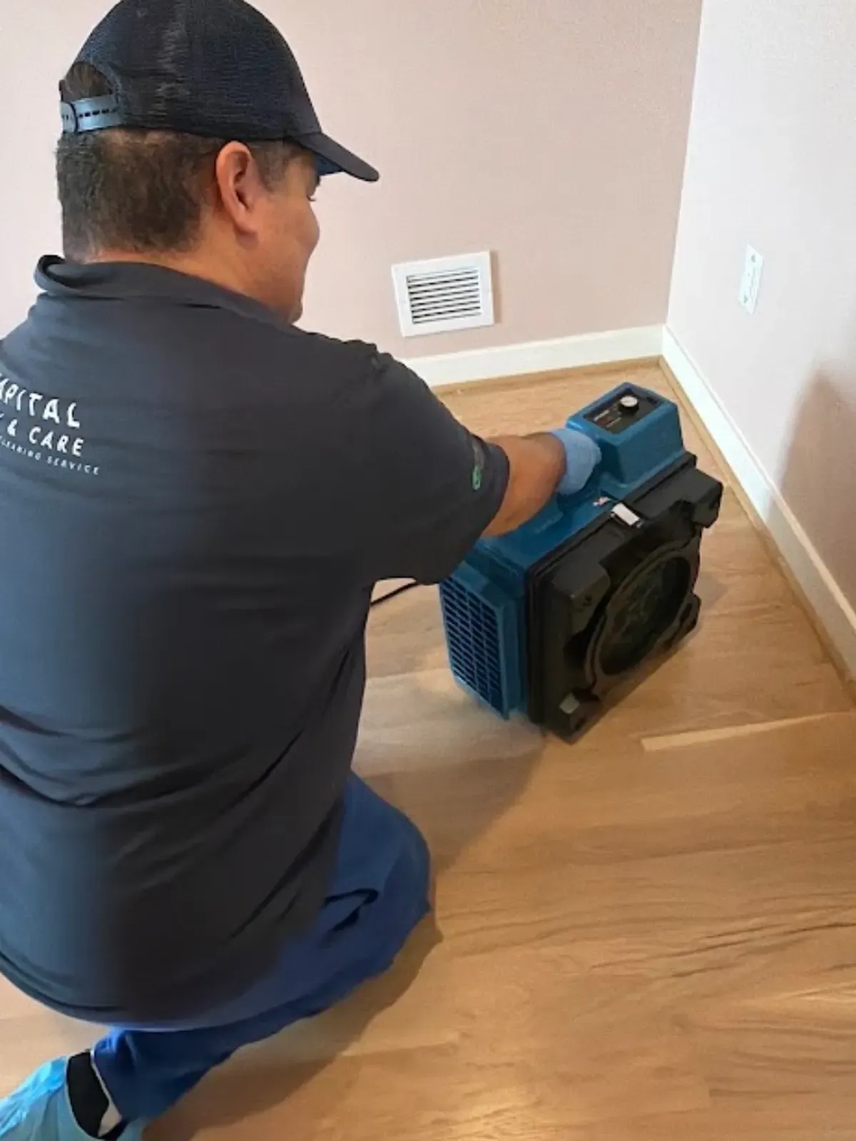 Capital Clean Care team member setting up a blue portable air scrubber beside a wall vent.