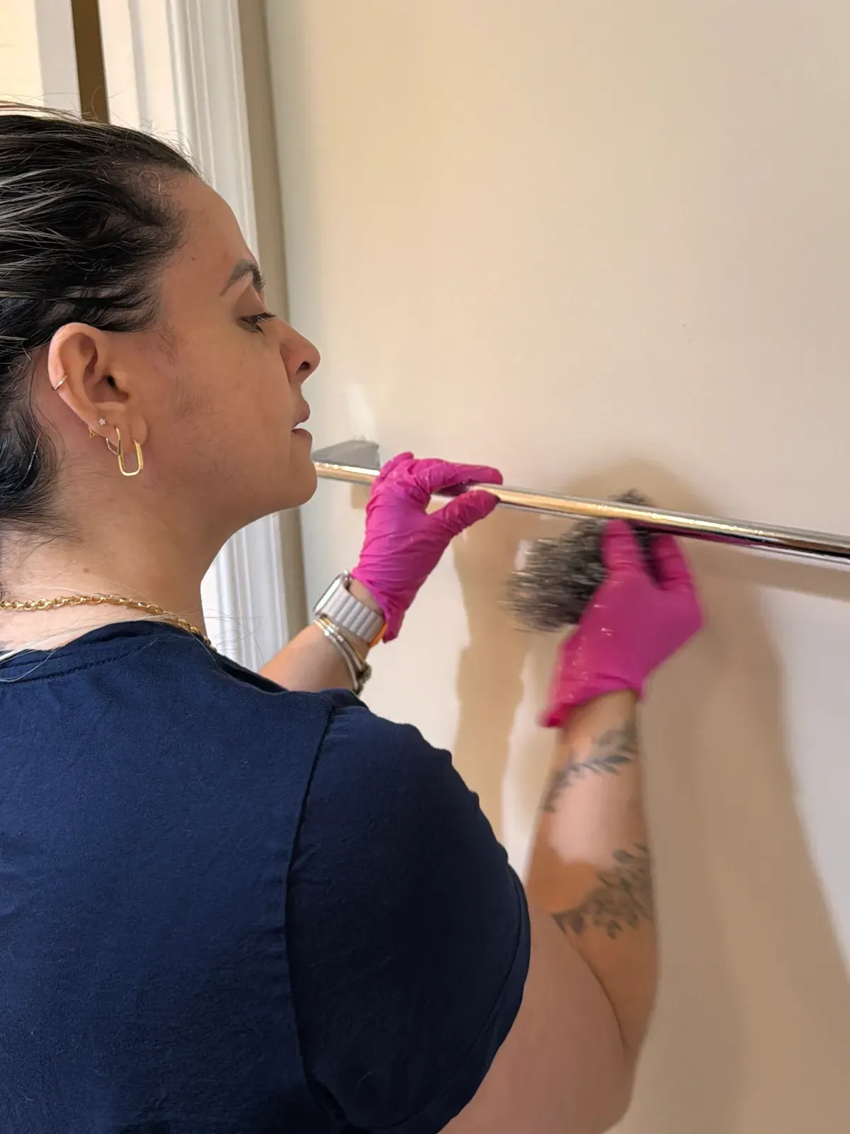 Team member detailing a chrome towel bar against a painted wall.