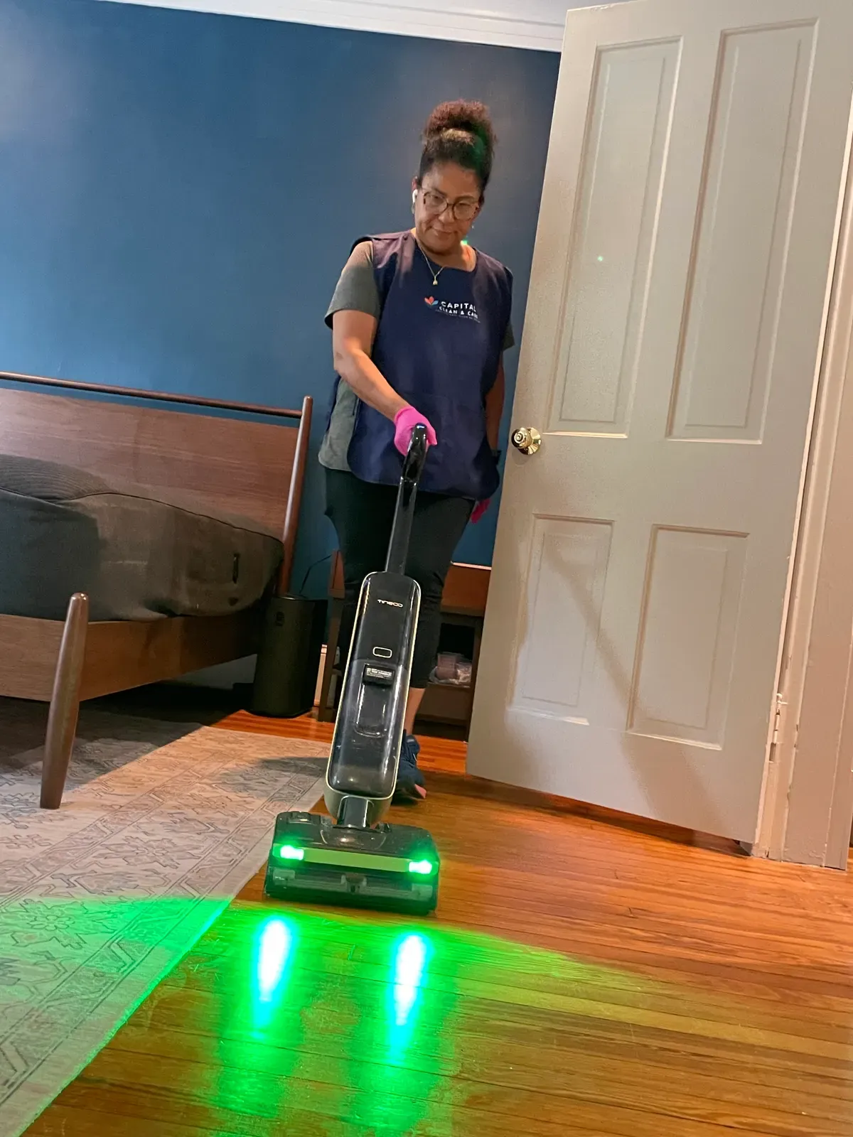 Team member using a floor cleaner with green lights on a wood floor.