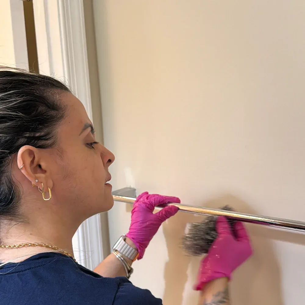 Team member hand-dusting a chrome towel bar with a duster