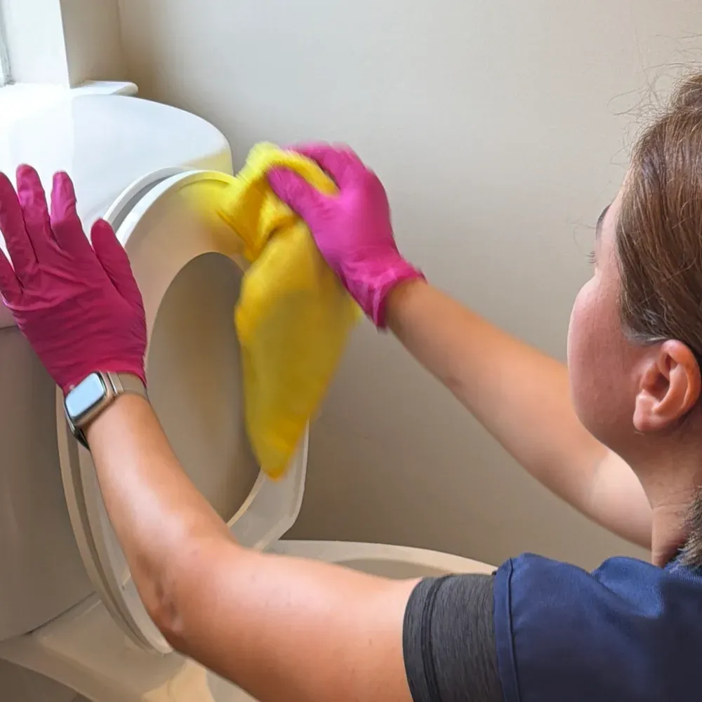 Technician wiping a toilet seat with a yellow microfiber cloth during the final pass
