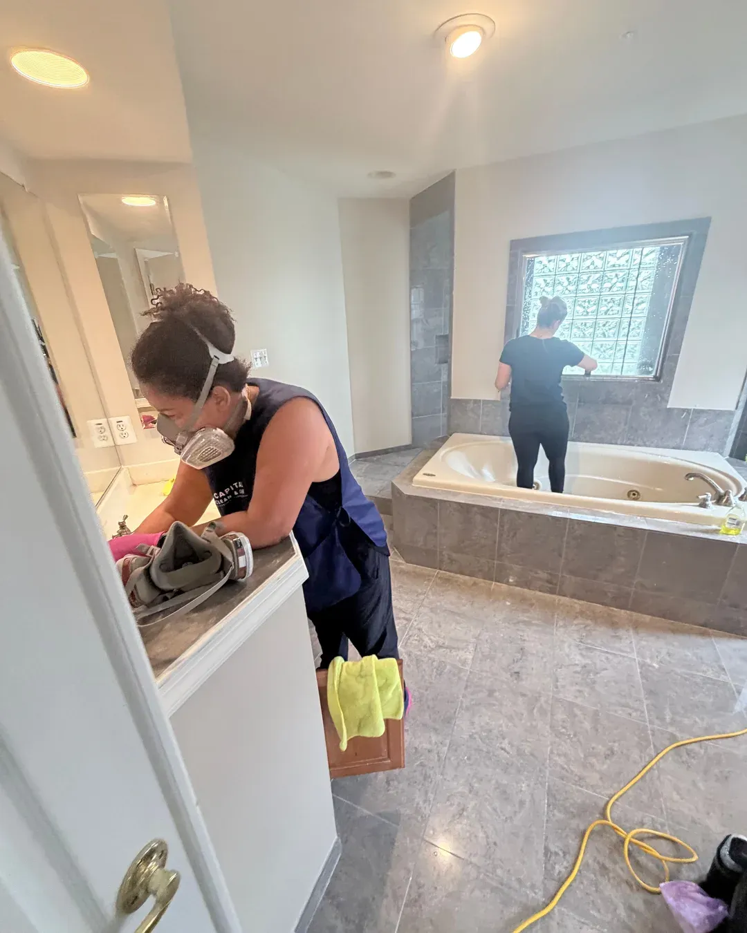 Technician in a respirator detail-cleaning the vanity while a teammate works on the soaking tub