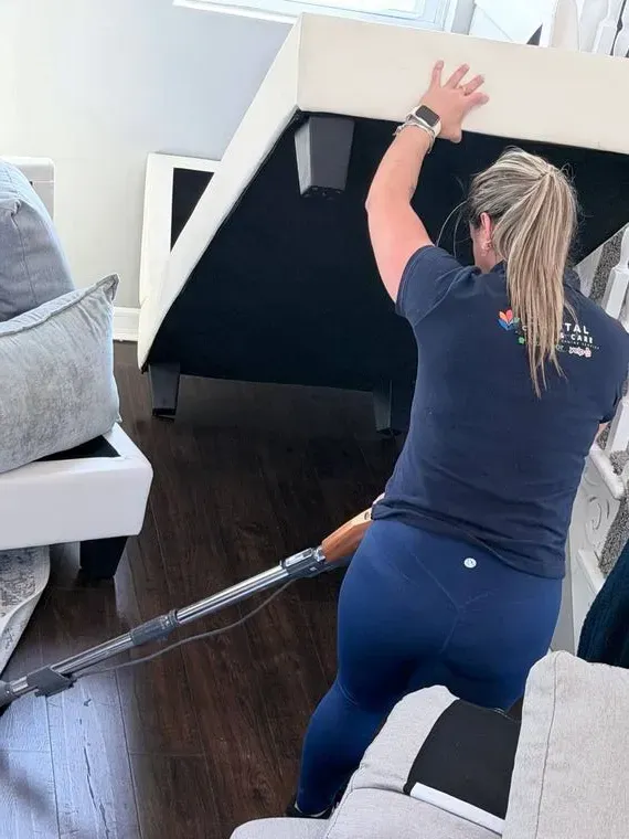 Capital Clean Care employee vacuuming upholstered furniture in a living room
