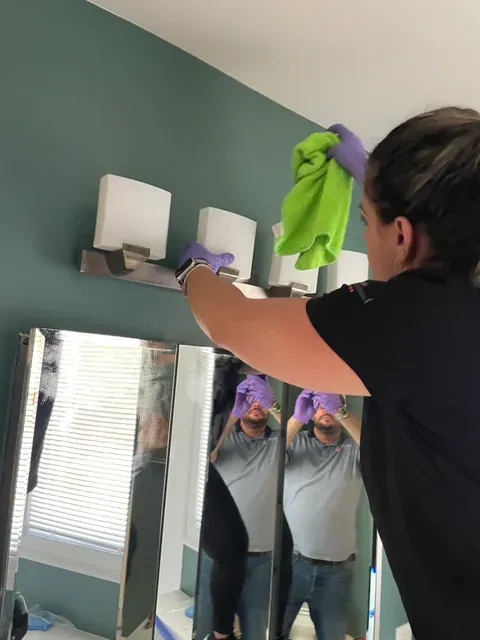 Capital Clean Care professional wiping bathroom light fixtures above a mirror during a Rockville cleaning visit