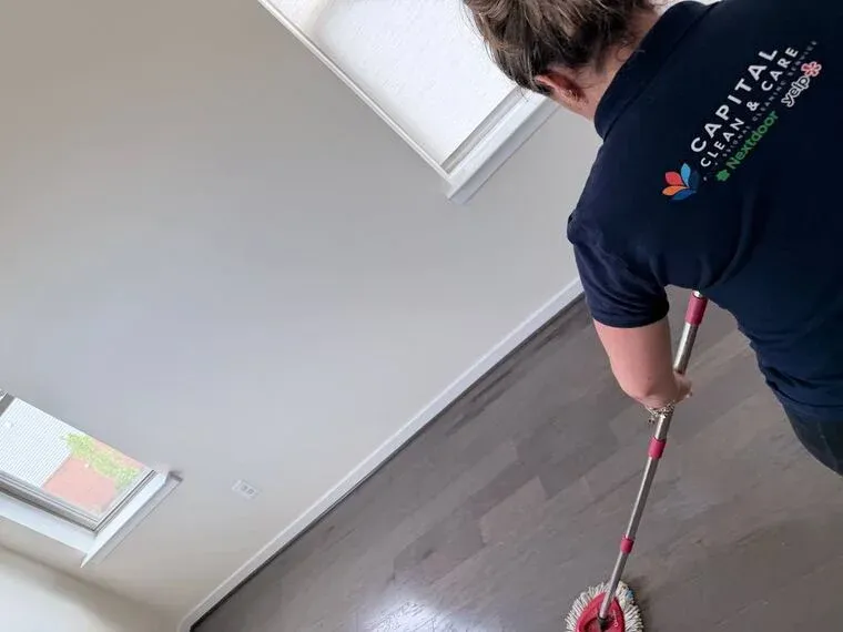 A Capital Clean Care team member damp-mopping a hardwood floor in a bright, uncluttered room