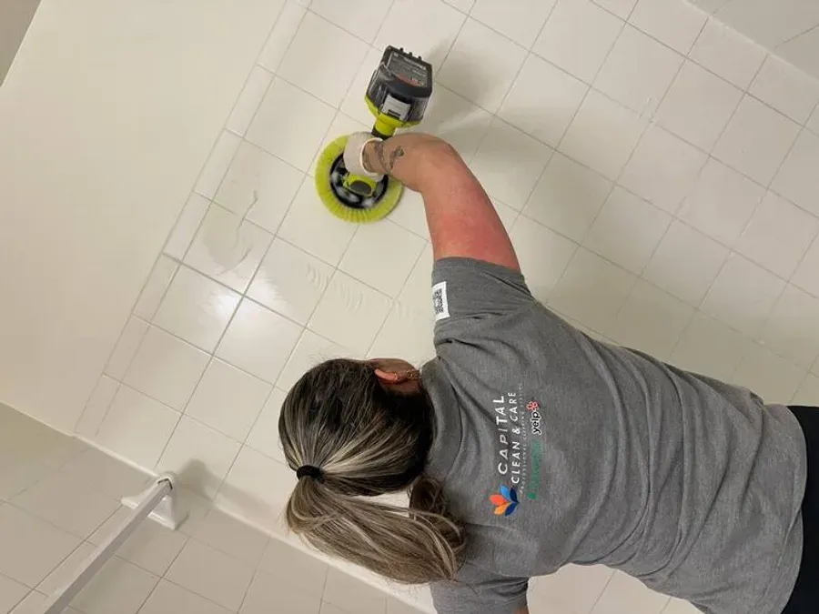 A Capital Clean Care team member power-scrubbing bathroom tile and grout during a professional bathroom cleaning