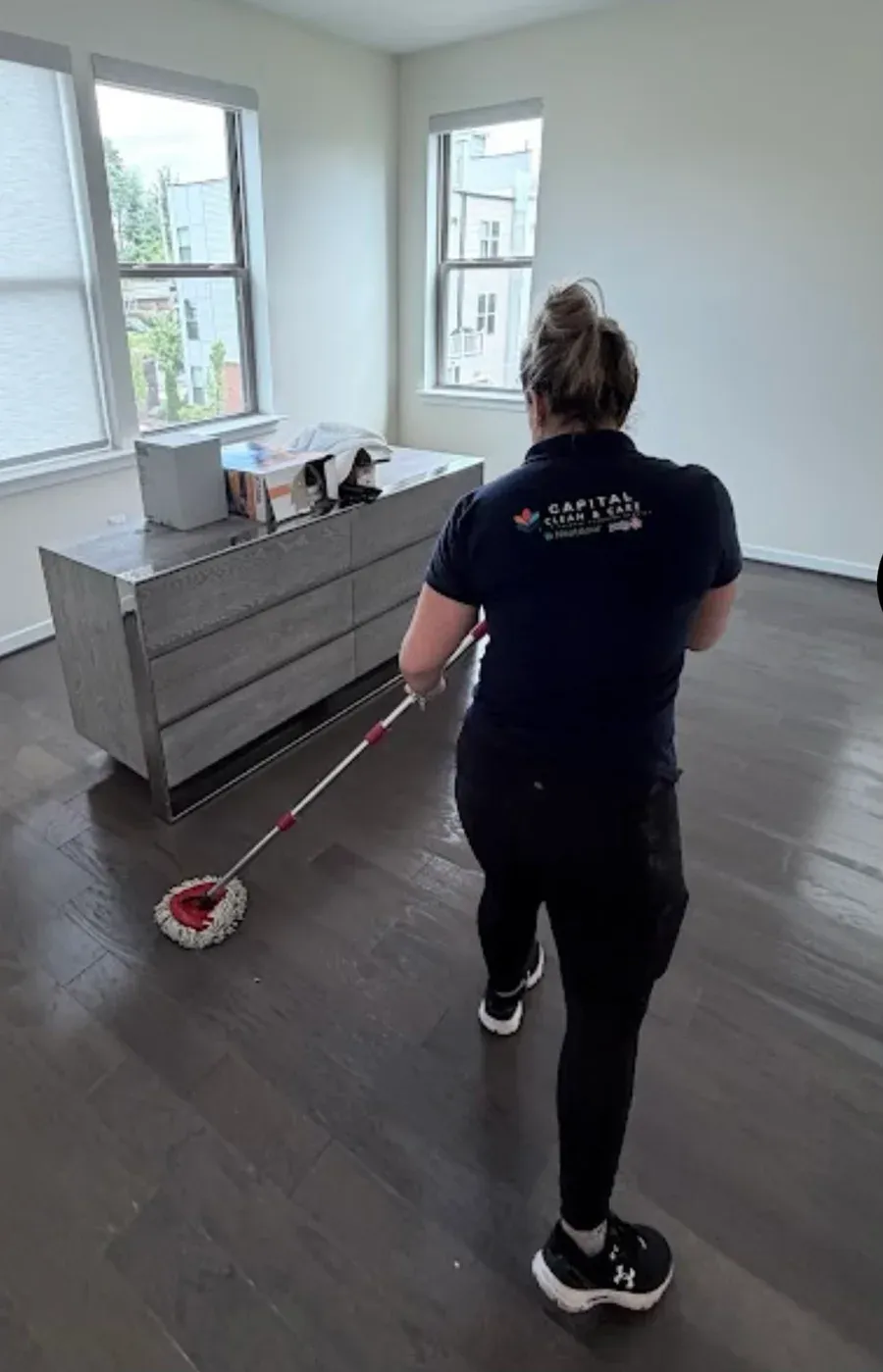A Capital Clean Care team member in a branded navy uniform cleaning a client's home in Maryland, DC & Northern Virginia