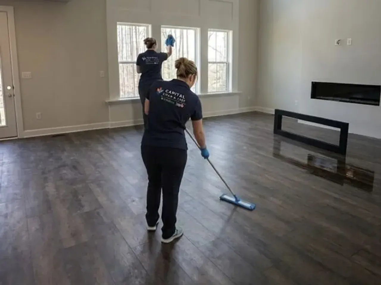 A Capital Clean Care team in navy uniforms cleaning the floors and windows of a bright, spacious living area in a DMV home