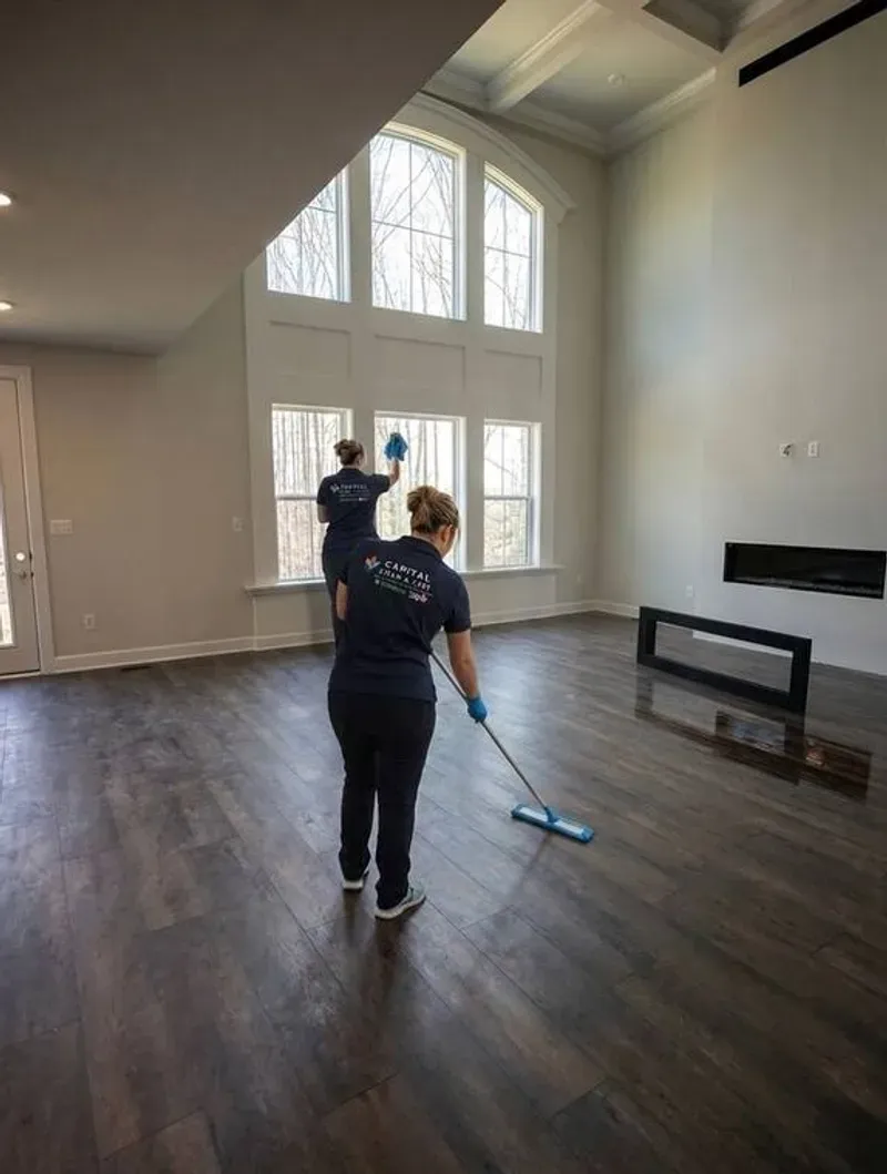 A Capital Clean Care team cleaning the windows and floors of a bright, spacious living area