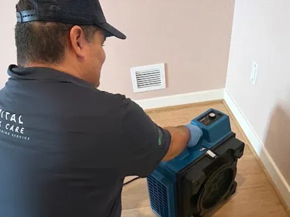 A uniformed Capital Clean Care team member setting up air-handling equipment against the baseboard of an empty renovated room