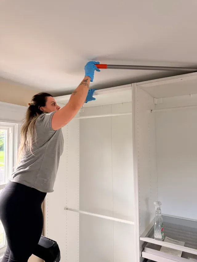 A Capital Clean Care team member reaching the ceiling with an extension tool over a newly installed closet