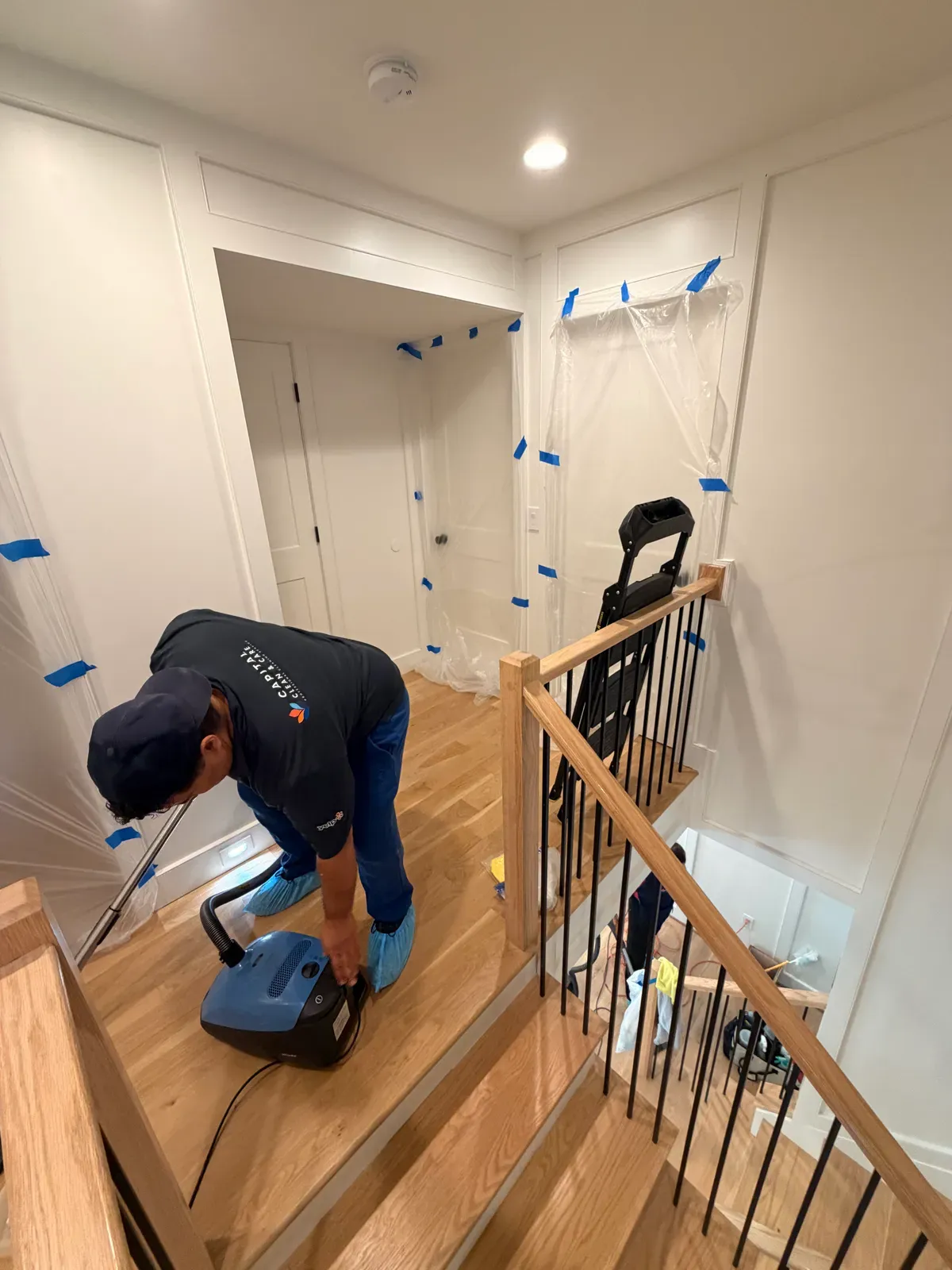 Capital Clean Care employee in shoe covers vacuuming new oak stairs while the walls are still masked from the renovation