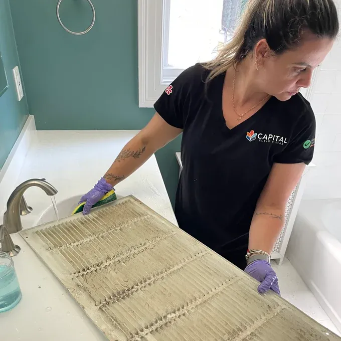 Team member washing a dust-covered HVAC return cover in a sink.